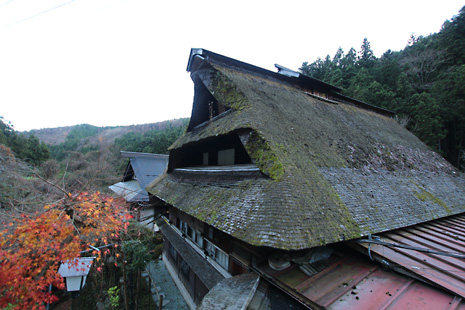 大きな茅葺屋根の古民家の写真。屋根のてっぺんの傾斜が急で、武士の兜に似た形をしています。